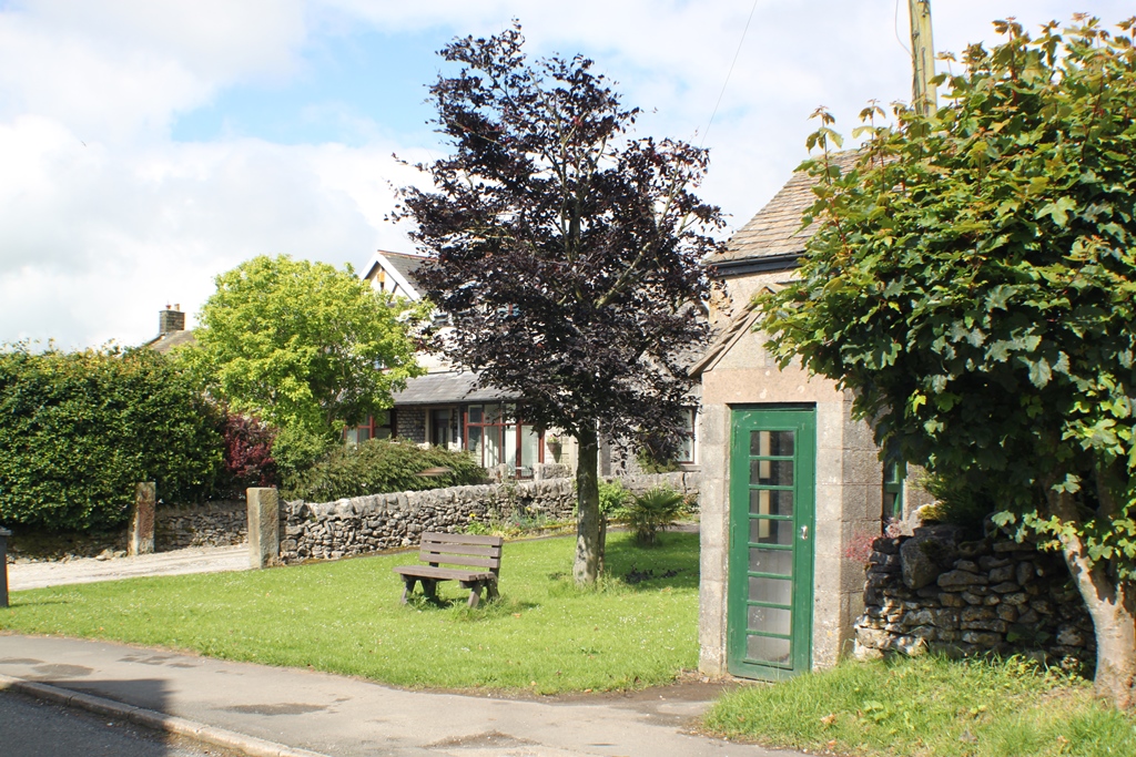 A small village green with a bench and a phone kiosk