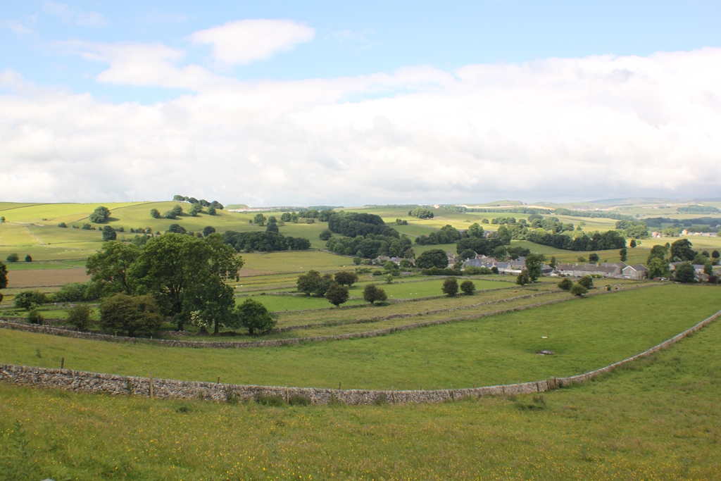 A view of fields sloping downwards to a village in the distance